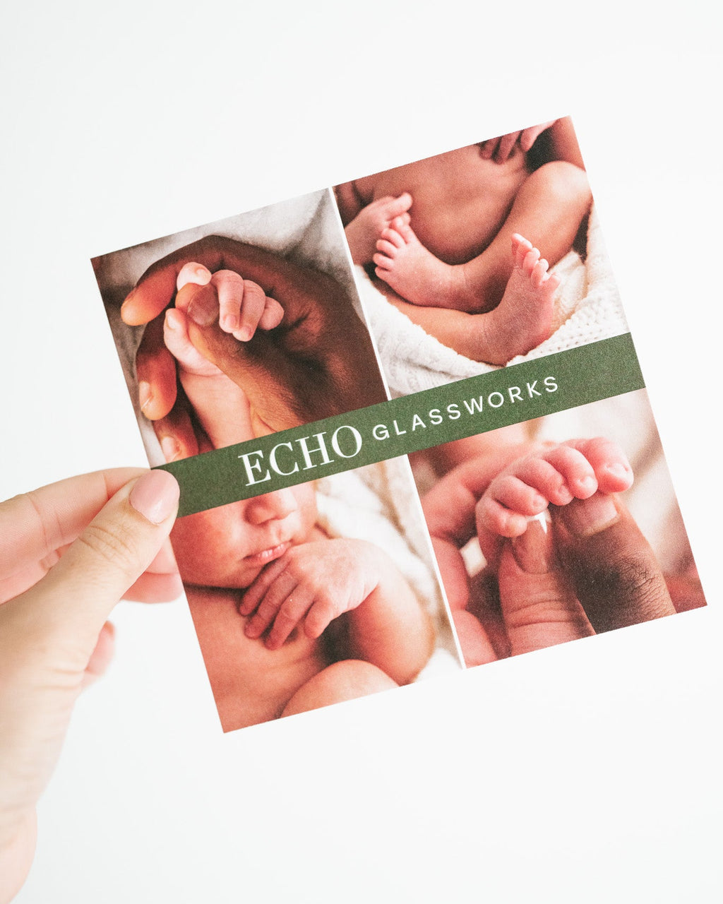 A hand holds a square printed card featuring four photos of baby hands and feet, with a dark green horizontal band reading “ECHO GLASSWORKS” on a white background.